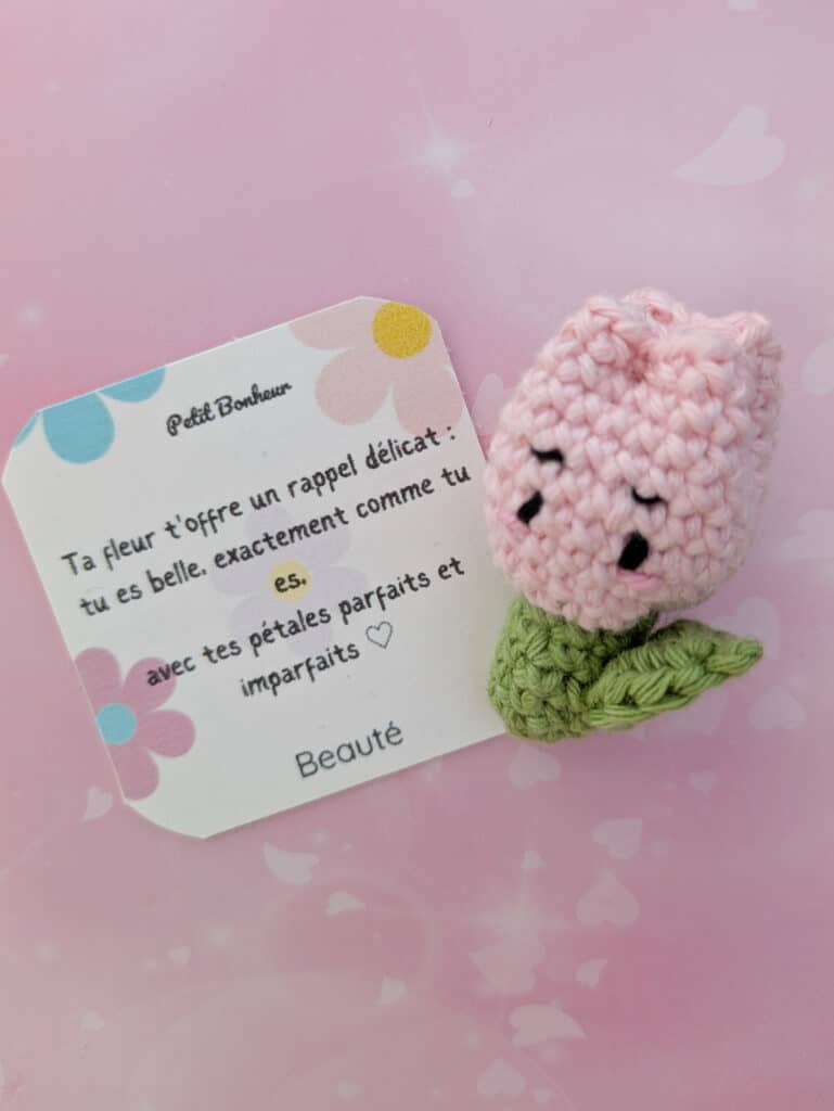 Un crochet de tulipe rose clair avec une tige et des feuilles vertes. La tulipe a un visage souriant avec des yeux noirs.