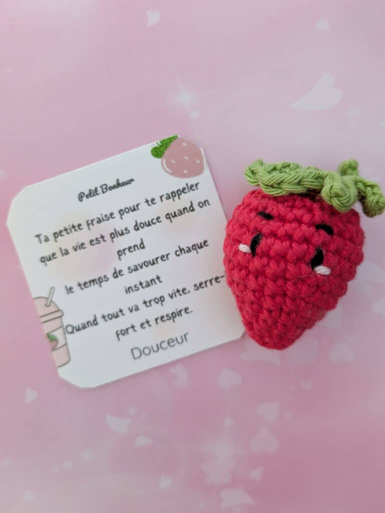 Une fraise crochetée avec une tige verte et des détails blancs. Une carte avec du texte français et une illustration de fraise est également présente.