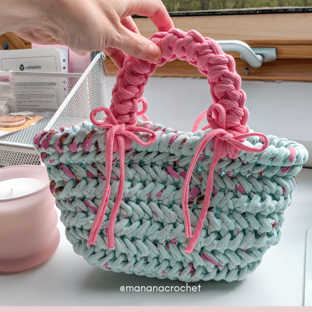 Sac au crochet fait main avec du fil trapilho couleur menthe avec une anse rose girly tenu par une main